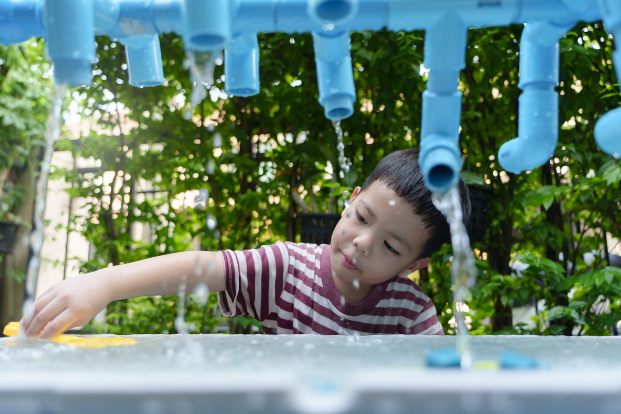 Young Asian boy with a striped shirt is engaged in a water play activity at a garden station, enjoying the splashes.